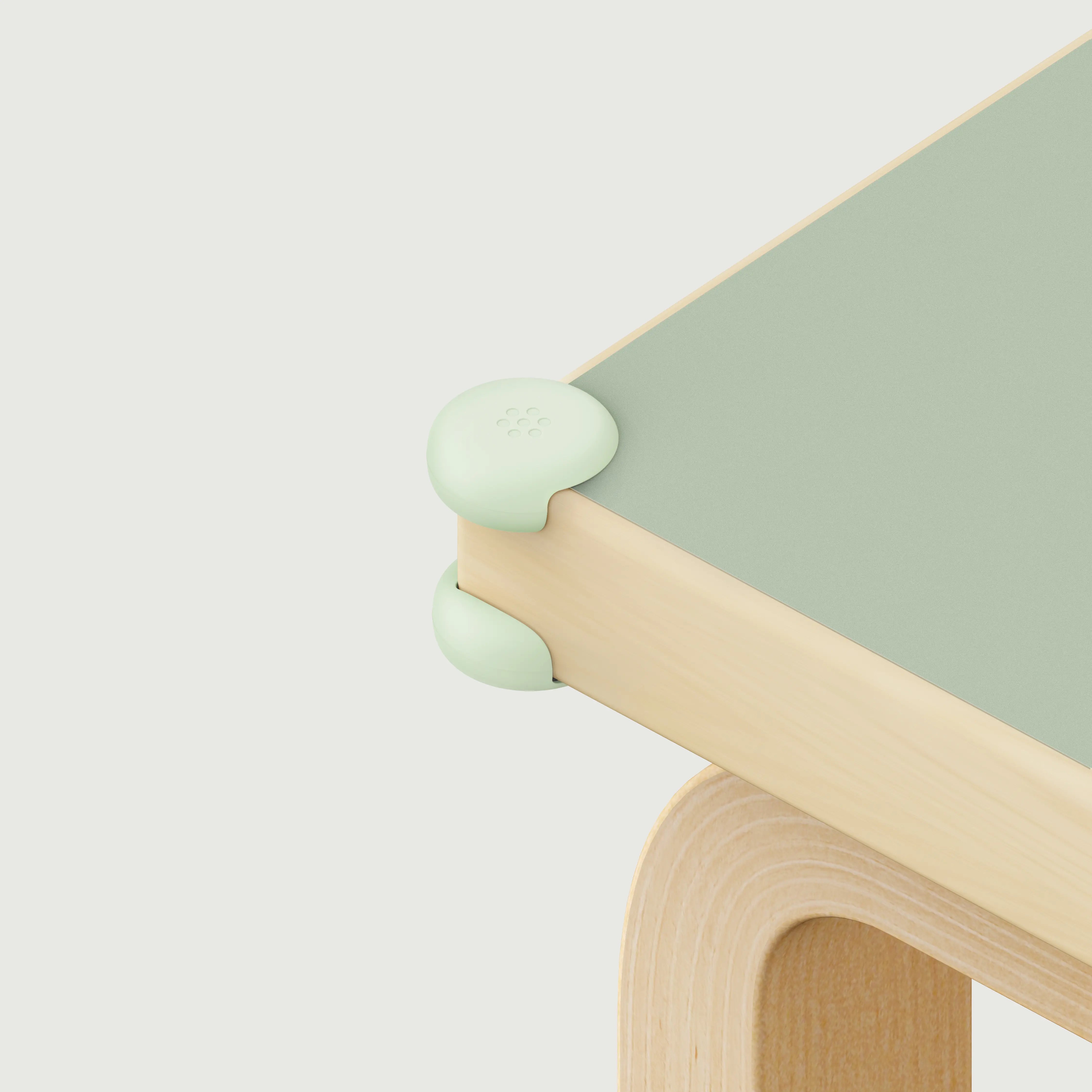 Pom Corner Protector — soft silicone babyproofing guard for sharp furniture corners on a green table